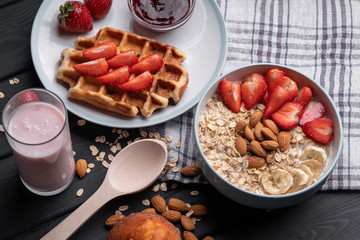 Tasty breakfast. Fresh oatmeal with crispy Belgian waffle with strawberries. Berry yogurt. Morning food on black table background