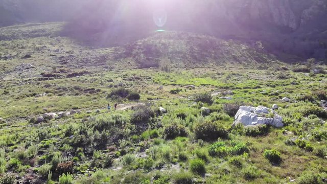 Aerial footage of two female runners on a trail at the foothills of a mountain along a river