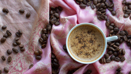 White coffee cup and coffee beans around it with traditional fabric background