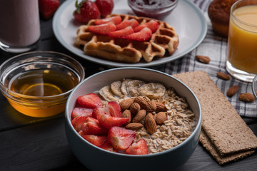 Oatmeal. Breakfast. Food. Muesli. Snack. Morning meal. Fresh waffles. Strawberry, honey, jam, almond and muffin on black table background