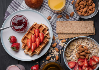 Breakfast. Morning meal set. Delicious oatmeal granola with berries, nuts and honey. A crispy waffle topped with strawberry jam. On a black table background. Top view