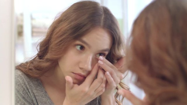 Young woman removing contact lenses for eyes at mirror in home bathroom