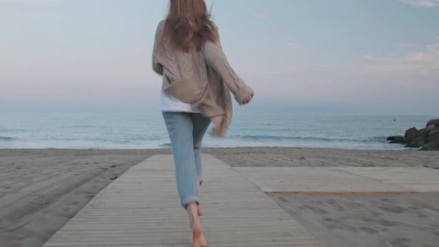 Unrecognizable woman running in the summer sunset along the sunny  shore, Carefree girl takes off her flip flops and runs in the sand