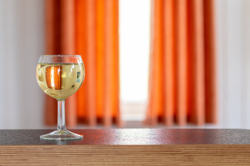 Single glass of white wine standing on a sideboard in front of a window with sunshine 