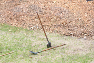 Two shovels in the grass next to some mulch in a community park.
