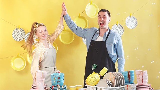 Beautiful active young hardworking couple is giving high five and smiling in kitchen, isolated yellow background, good job.