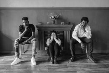 Kidnapped woman concept. Despair young girl sitting on floor betwen two african men and covering her crying face with hands. Two serious dark skinned gangsters guarding female hostage in empty room.