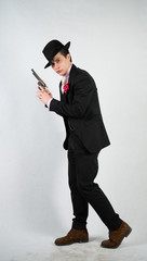 young man in a formal suit and hat with a gun in his hands on a white background in the Studio alone