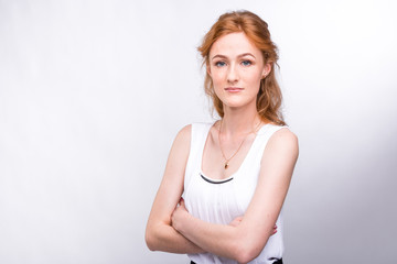 Portrait of a beautiful young woman of European, Caucasian nationality with long red hair and freckles on her face posing on a white background in the studio. Close-up student girl in a white blouse