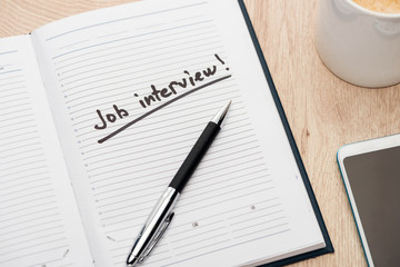 notebook with pen and job interview lettering on wooden table near smartphone and coffee cup