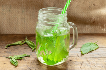 nettle herbal tea at jar on a wooden background. fresh medicine nettle. background decorating with nettle leafs. traditional herbal medicine concept.