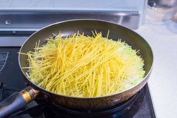 fry pan with raw spaghetti pasta cooking on boiled water.