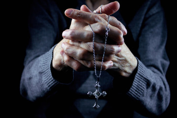Hands of an old woman holding a cross