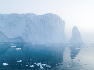 Fototapeta na wymiar The glaciers are melting on arctic ocean in Greenland. Big glaciers day by day broking and dangerous for world climate system. Shooting day was foggy weather and glaciers didn't look clear. 