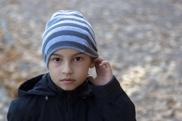 Close-up portrait of a poor child with hearing problems, holding his hand near his ear, showing me...