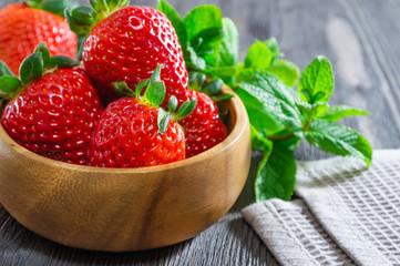 Delicious fresh strawberries in wooden bowl and mint leaves on wooden background.