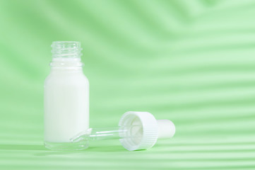 Natural cosmetics: serum with dropper on green background with shadow.