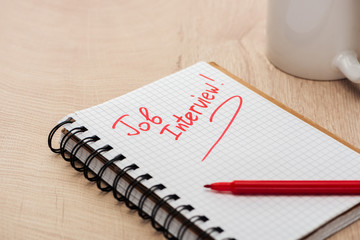 notebook with job interview lettering on wooden table with red marker and cup