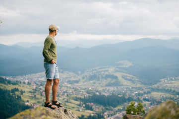 Fototapeta na wymiar Lifestyle summer portrait of successful man standing on top of mountaing with beautiful landscape in front. Male traveler enjoying nature view from highest peak at hill.