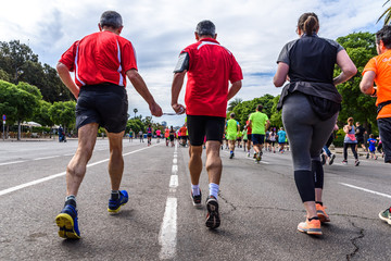 Valencia, Spain - May 19, 2019: Mature man blind runner and his companion joined by a cord to guide him during an amateur competition surrounded by other runners reaching the finish line.
