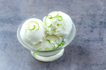 scoops of lime ice cream with lemon zest, mint, in a cup on slate
