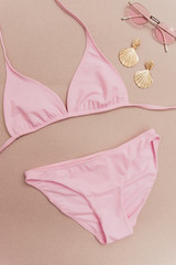pink separate swimsuit on a beige background with gold earrings and sunglasses. concept of sea vacation and vacation.