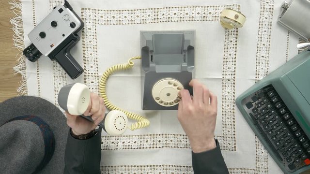 Old time filmmaker producer dials a number on a rotary phone. 50's 60's 70's vintage scene. Historical reenactment concept.