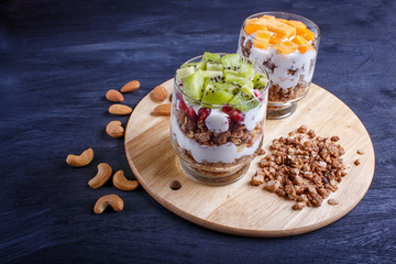 dessert with greek yogurt, granola, almond, cashew, kiwi and persimmon on wooden background.