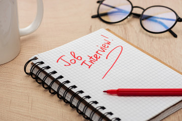 notebook with job interview lettering on wooden table with red marker, glasses and cup