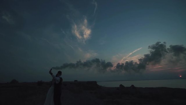 loving couple - young groom and beautiful bride at sunset , silhouette using hand flare or fusee smoke