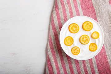 greek yogurt with kumquat pieces in a white plate on a white wooden background