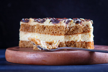 a piece of cake with milk and butter cream cutted with spoon on a wooden kitchen board, black background..