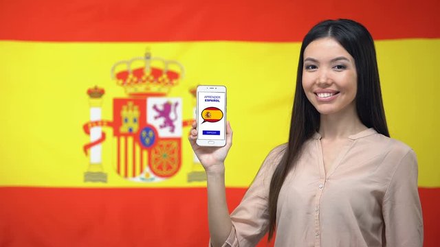 Girl holding smartphone with language study app, Spanish flag on background