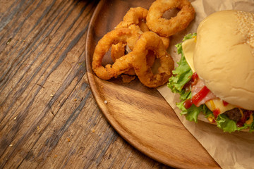 Cheese burger with onion rings on round wooden plate with copy space on the left. 
