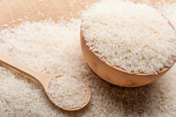Jasmine rice in a wooden bowl,  spoon on wooden background, organic and healthy concept.