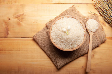 Top view of jasmine rice with jasmine flower on top in a wooden bowl,  spoon burlap sack and  ear of rice