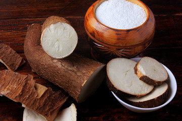 tapioca flour in wooden bowl on rustic wooden table, next to cut and sliced cassava