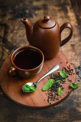 Mint tea in brown ceramic cup and teapot on a warm wooden background with tea brew and mint leaves.