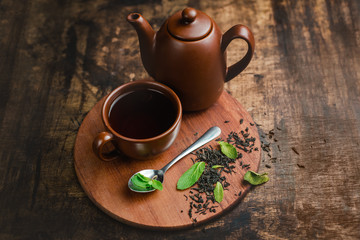 Mint tea in brown ceramic cup and teapot on a warm wooden background with tea brew and mint leaves.