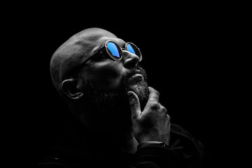 Pensive bald man with a gray beard in sunglasses on a dark background