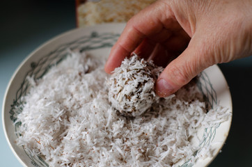 raw food sweets roll in coconut flakes in a light plate with female hands