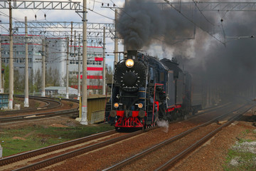 Obraz premium An old steam train in clouds of smoke rides by rail