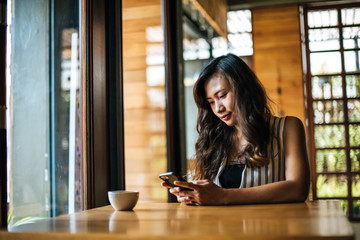 Woman Sitting and playing her smart phone at cafe