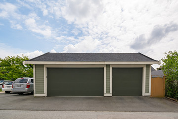 Detached wide garage for three cars parking. Back yard garage with two cars parcked beside on cloudy sky background