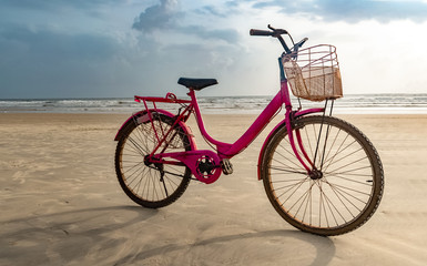 Fototapeta premium Pink colored old ladies bicycle parked on the isolated beach after cycling. A fun filled healthy activity and a must to do on the beach.