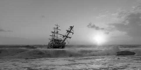 Sailing old ship in storm sea against dramatic sunset