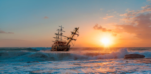 Sailing old ship in storm sea against dramatic sunset