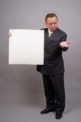 Portrait of mature Asian businessman against gray background