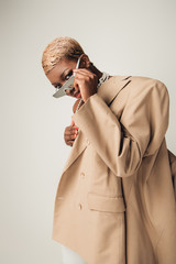 stylish african american girl with short hair posing in sunglasses and beige jacket isolated on grey