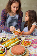 Young mother and child (daughter) eating food together. Vegan lunch, vegetarian dinner. Hands holds carrot salad and pancakes.